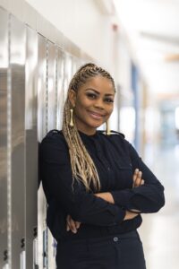 Female student smiling with arms crossed, leaning against a locker