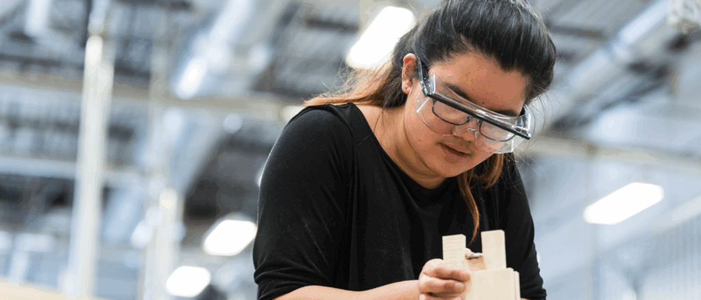 A student is wearing protection glasses and analyzing her work in a warehouse environment.