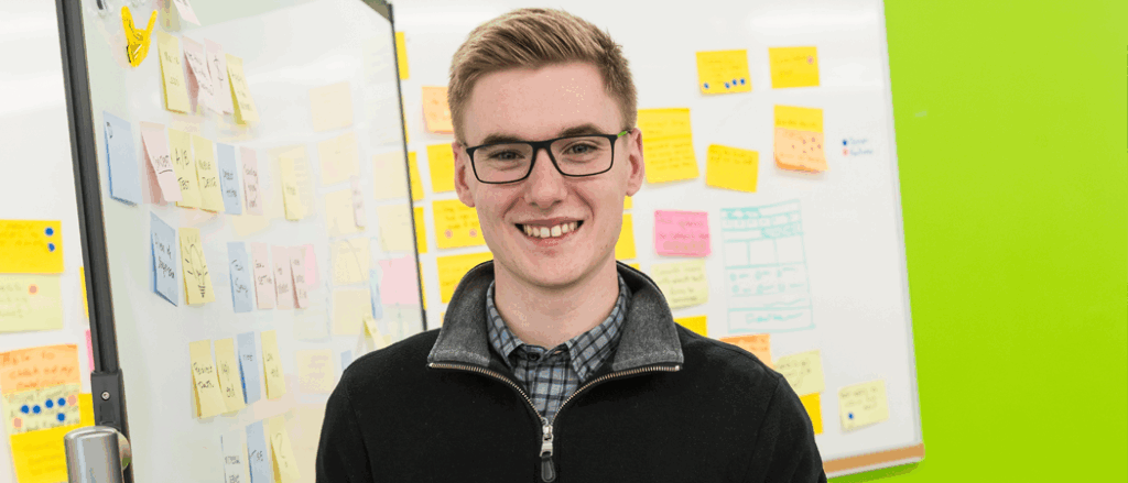 A student poses in front of a whiteboard filled with sticky notes.