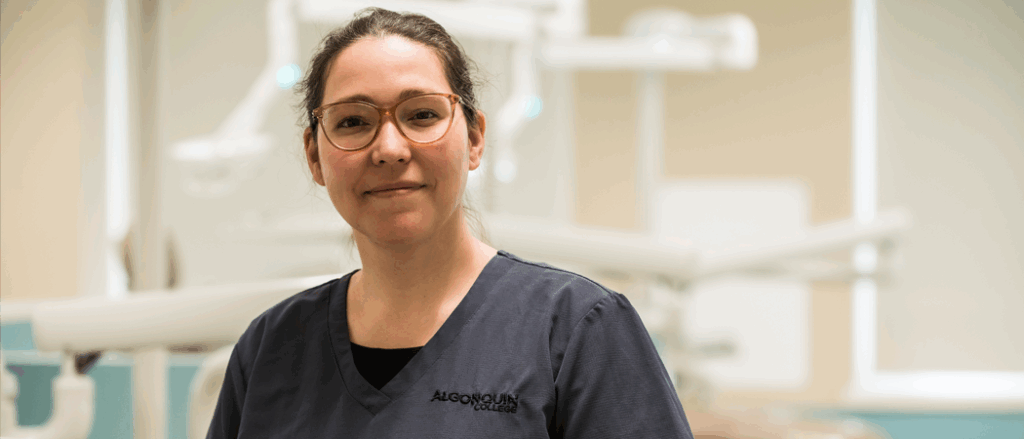 A student nurse poses for the camera in a hospital room.