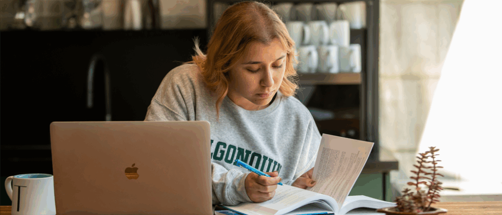 An Algonquin College student is sitting at a desk and studying her textbook.