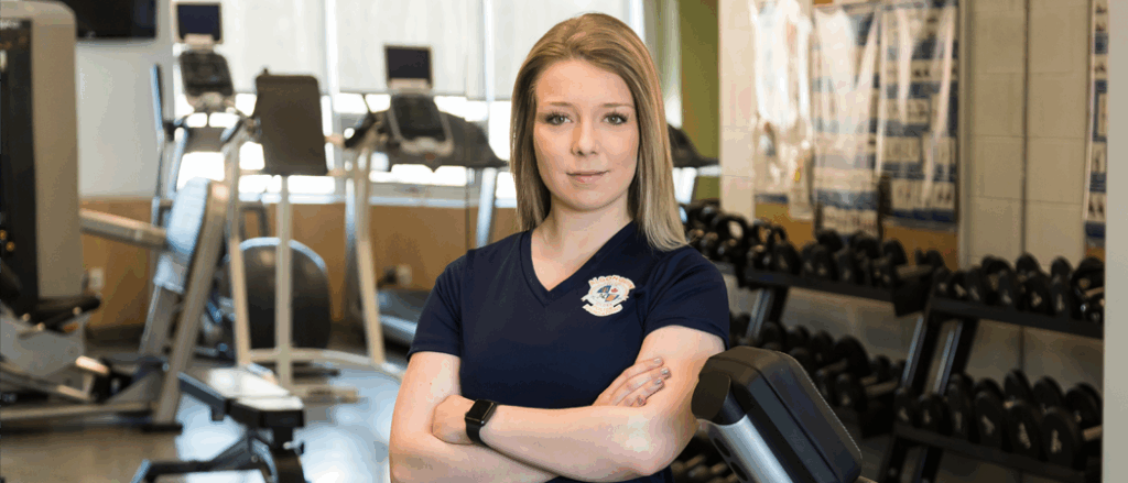 A student poses with her arms folded in front of gym equipment.
