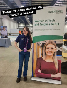 Hannah Hempinstall poses next to a Women in Tech and Trades banner.