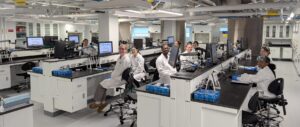 A group of students wearing aprons and safety glasses in a science lab.