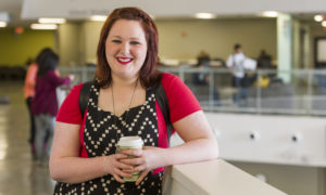 Caucasion female student smiling, holding coffee cup in Student Commons building
