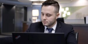 Male hotel apprentice wearing a suit, working behind a laptop