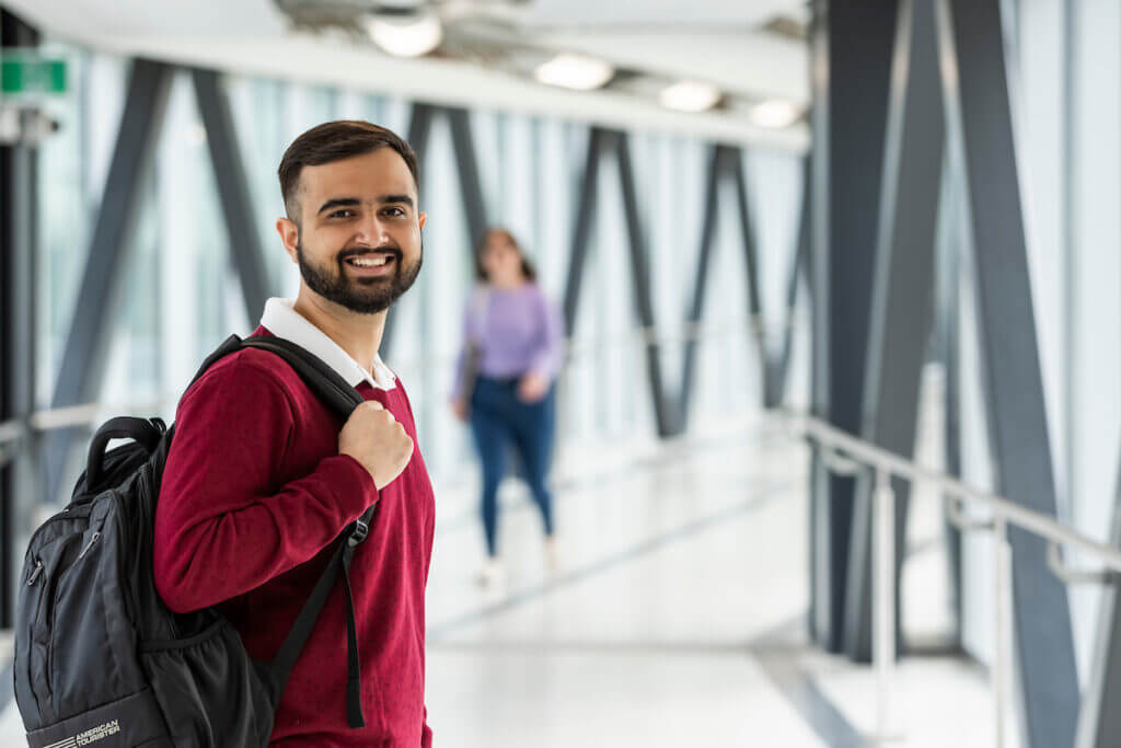 Male student smiling in hallway holding backpack