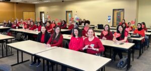 group of students sitting in a classroom, all wearing red, and smiling at the camera