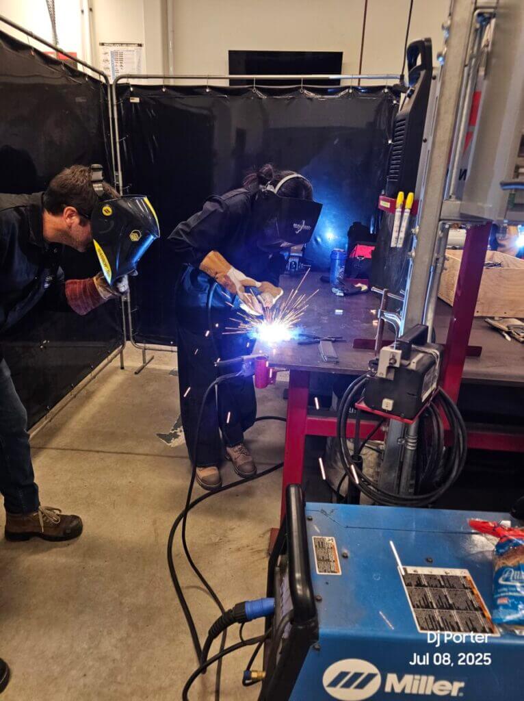 A student welding while an instructor watches nearby