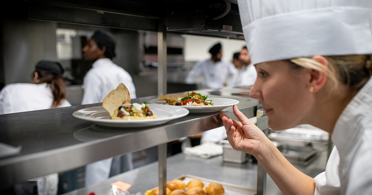 female culinary student picks up dishes from kitchen
