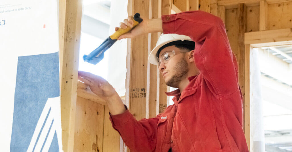 Male in red shirt is hammering a wood project.