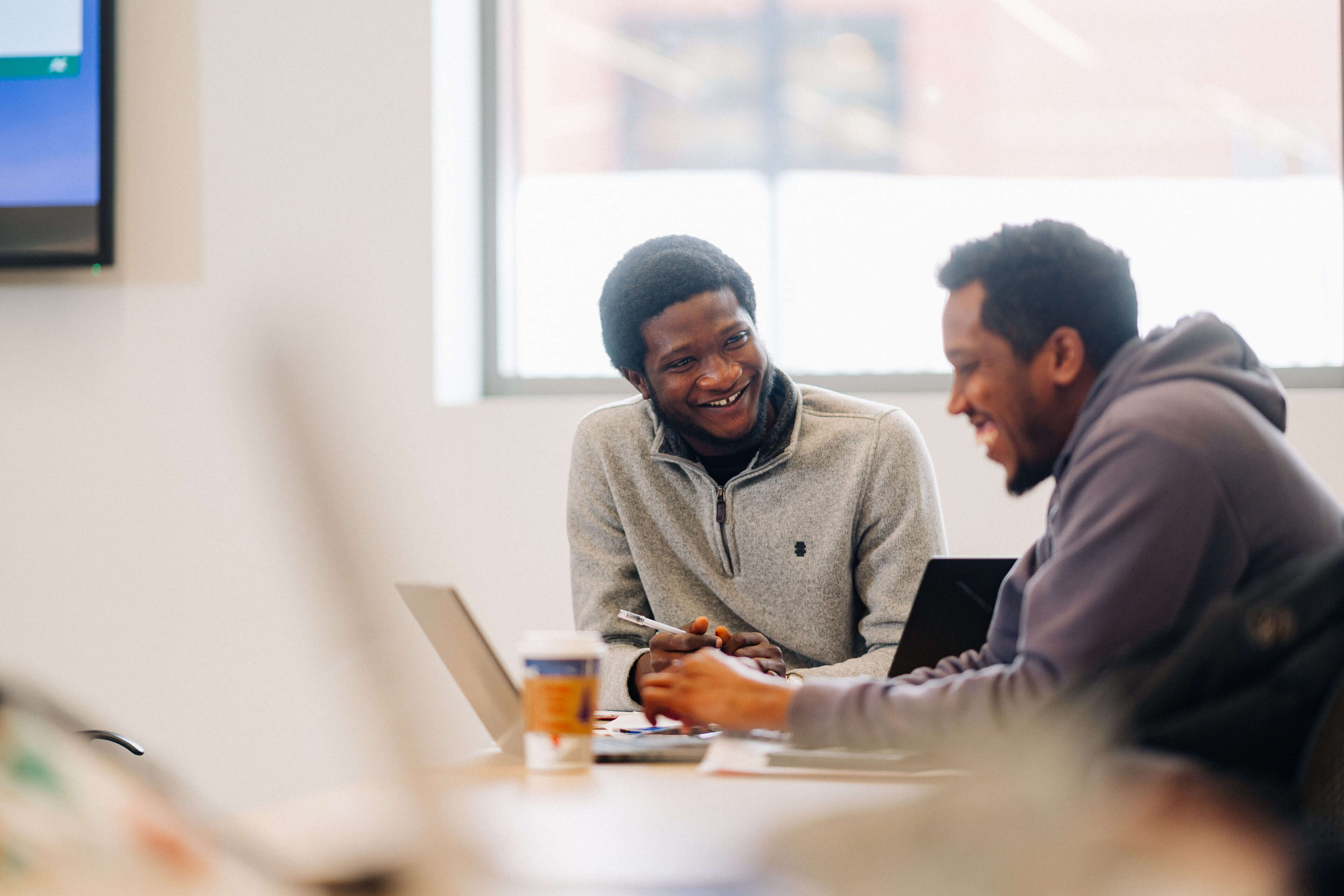 Two make students talk in front of a laptop.