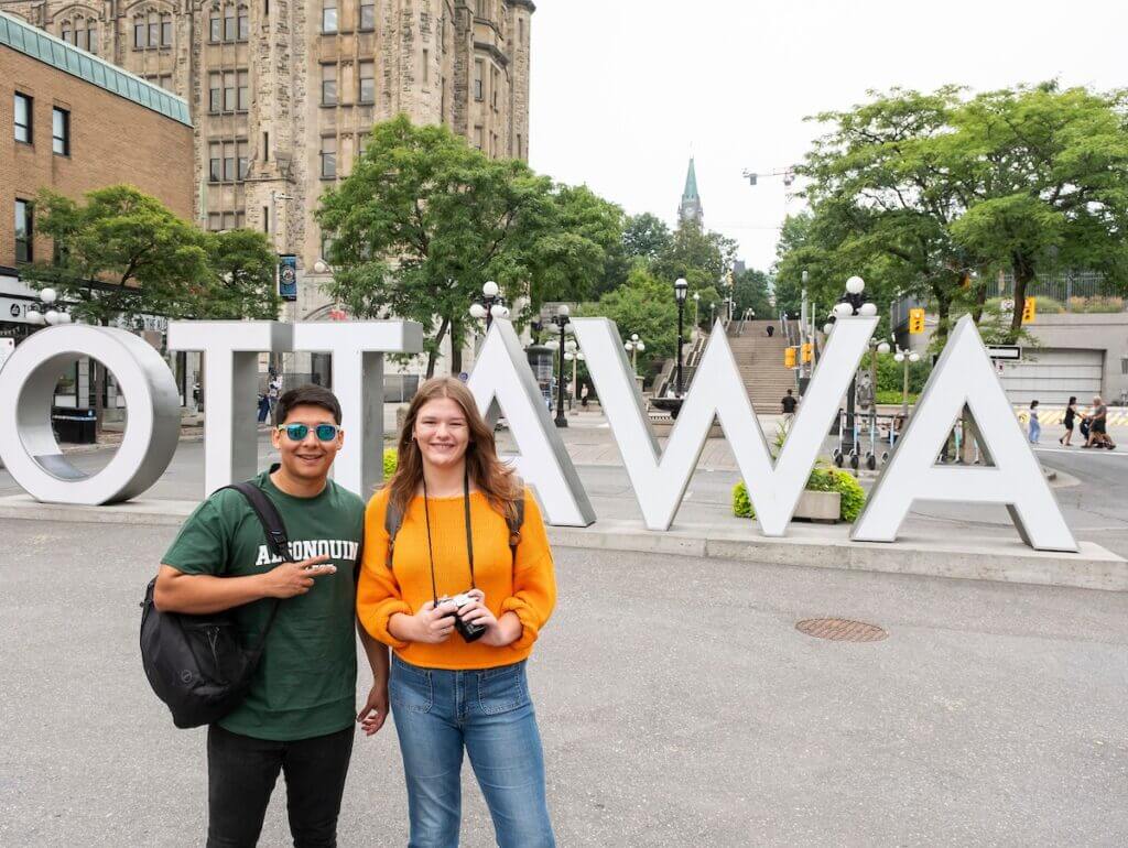 Male and Female student stand with camera in front of Ottawa sign in the Byward Market Ottawa Canada.