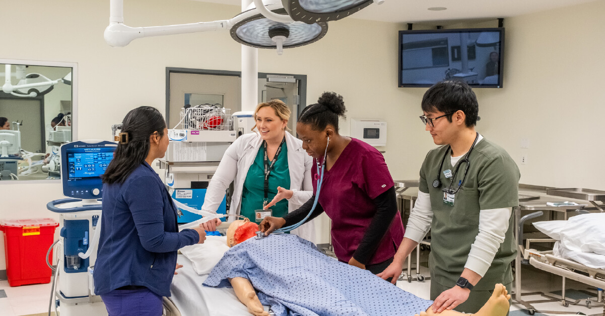 Students and faculty in a nursing lab learning with a nursing manikin. 