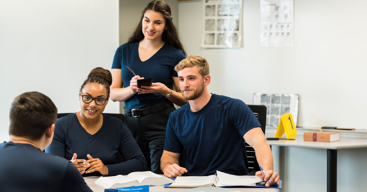 Four police foundations students in blue program shirts collaborate together.