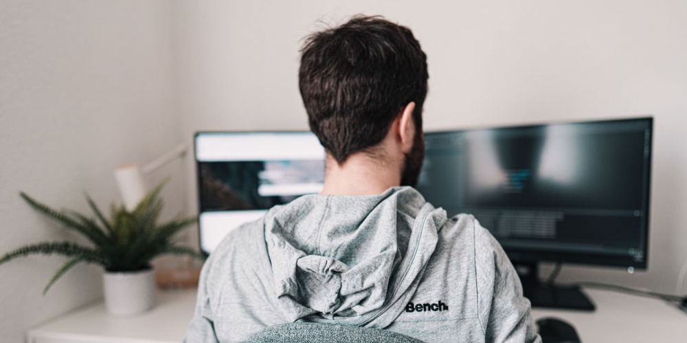 Young man sitting at a desk, facing two computer monitors