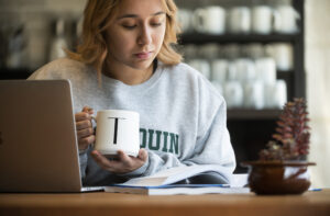 Algonquin College Online Student studying with book and computer in a coffee shop