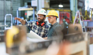 Two men working in a construction setting. One is pointing at something in the distance.