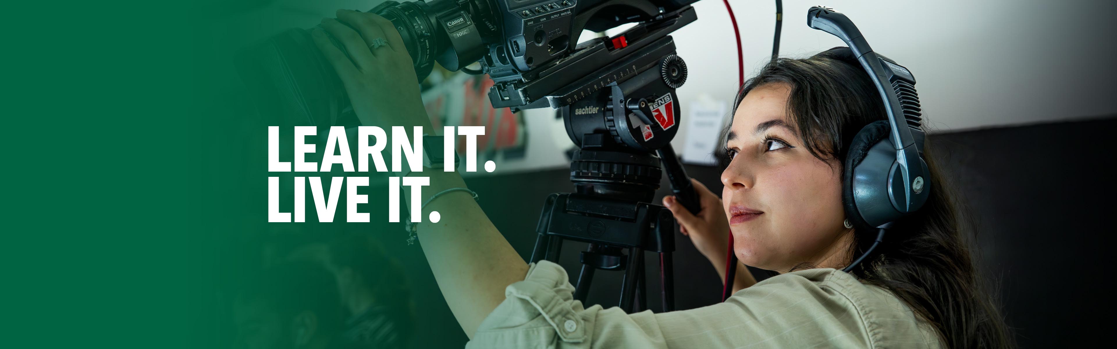 Student wearing a production headset while operating a professional video camera during hands-on media training.