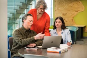 two students and professor reviewing project on laptop for the human services foundations program
