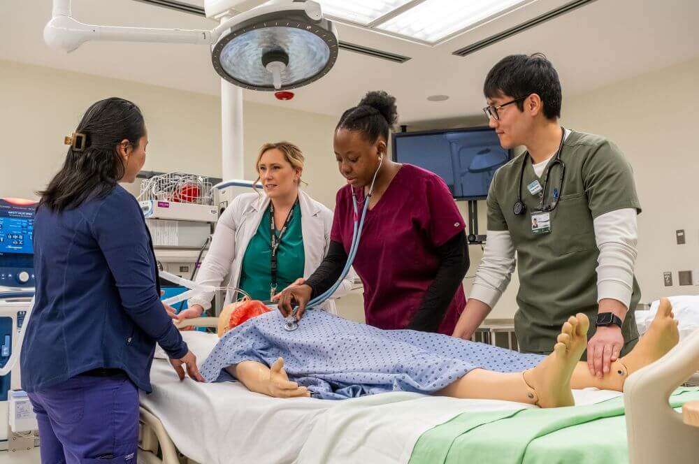 Two women and 1 man working with a female professor on a simulation mannequin in the operating room.