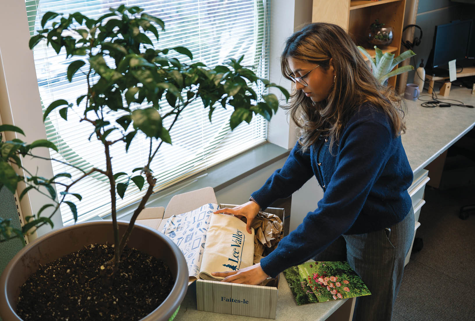 A woman is opening a box in an office setting, surrounded by potted plants and a TV. AI generated content