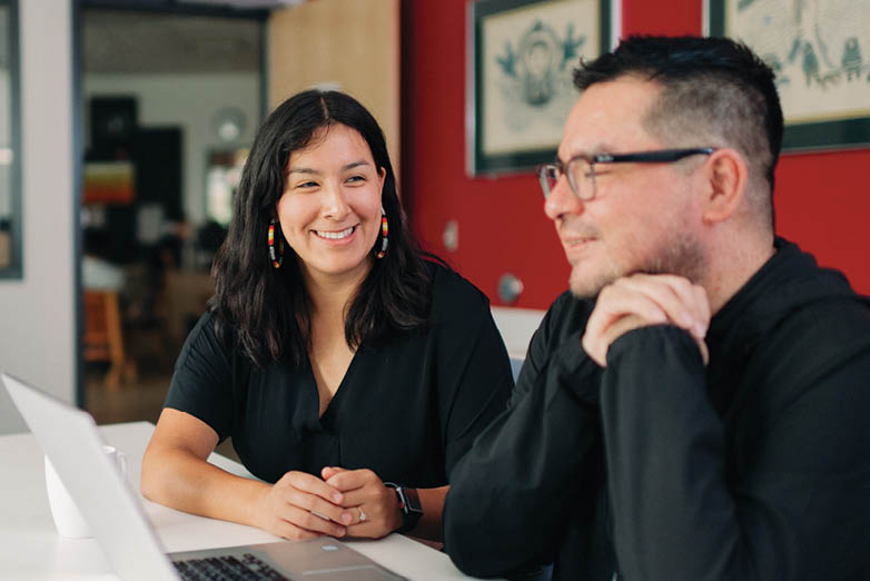 A man and a woman are sitting at a table with a laptop. AI generated content