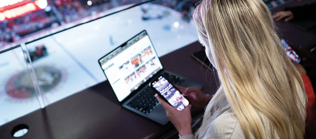 A woman is sitting in a booth at a hockey game, using her laptop. AI generated content