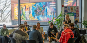 group of students gathered around elder playing a traditional drum