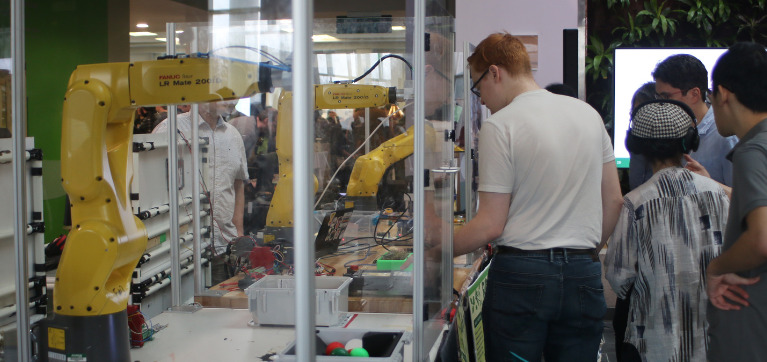 Robotic arms used in student projects are pictured with students around them.