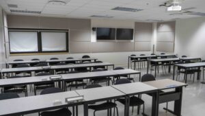 A room with tables and chairs, TVs at the back of the room and projector on the ceiling.