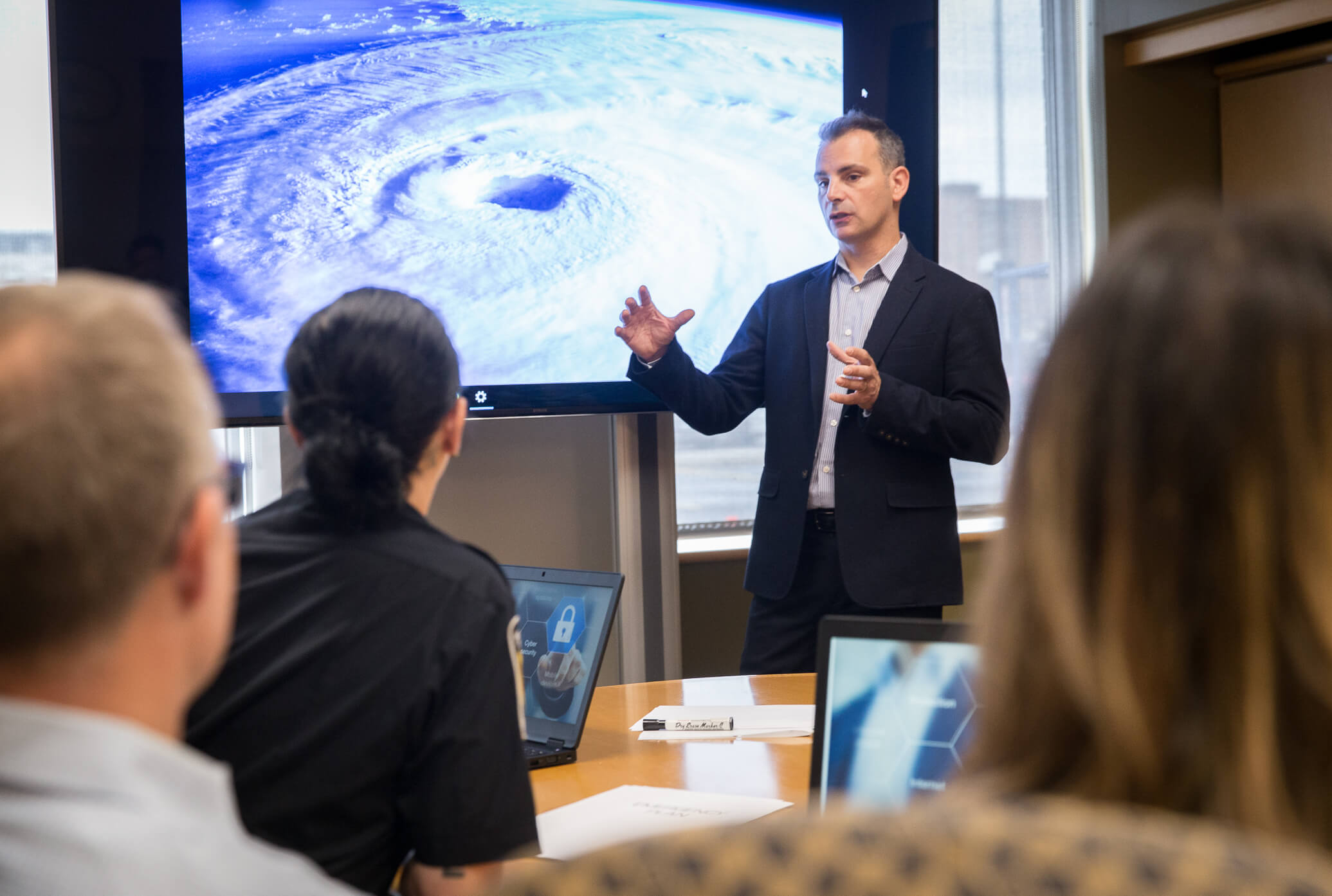 Bachelor of Public Safety Man presenting to the class on a natural disaster with a photo of a hurricane in the background.