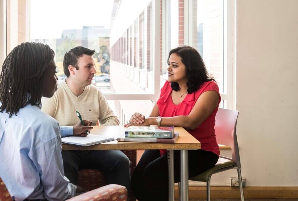 One man and two women sitting around a table practicing a scenario with a window in the background.