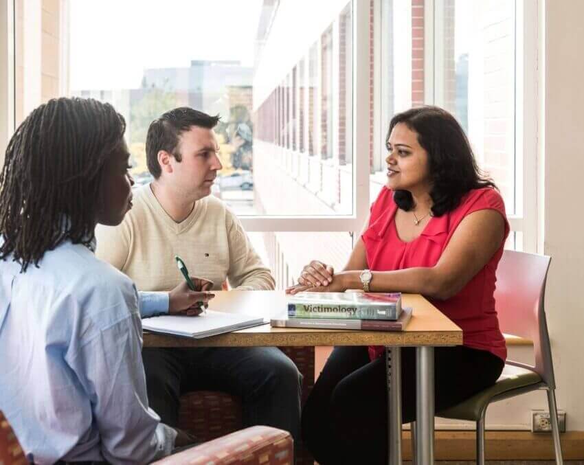 One man and two women sitting around a table practicing a scenario with a window in the background.