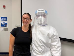 A female student standing next to a person in full Personal Protective Equipment gear.