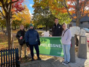 Students and staff standing in front of a green sign that says 24 Hours of Homelessness event