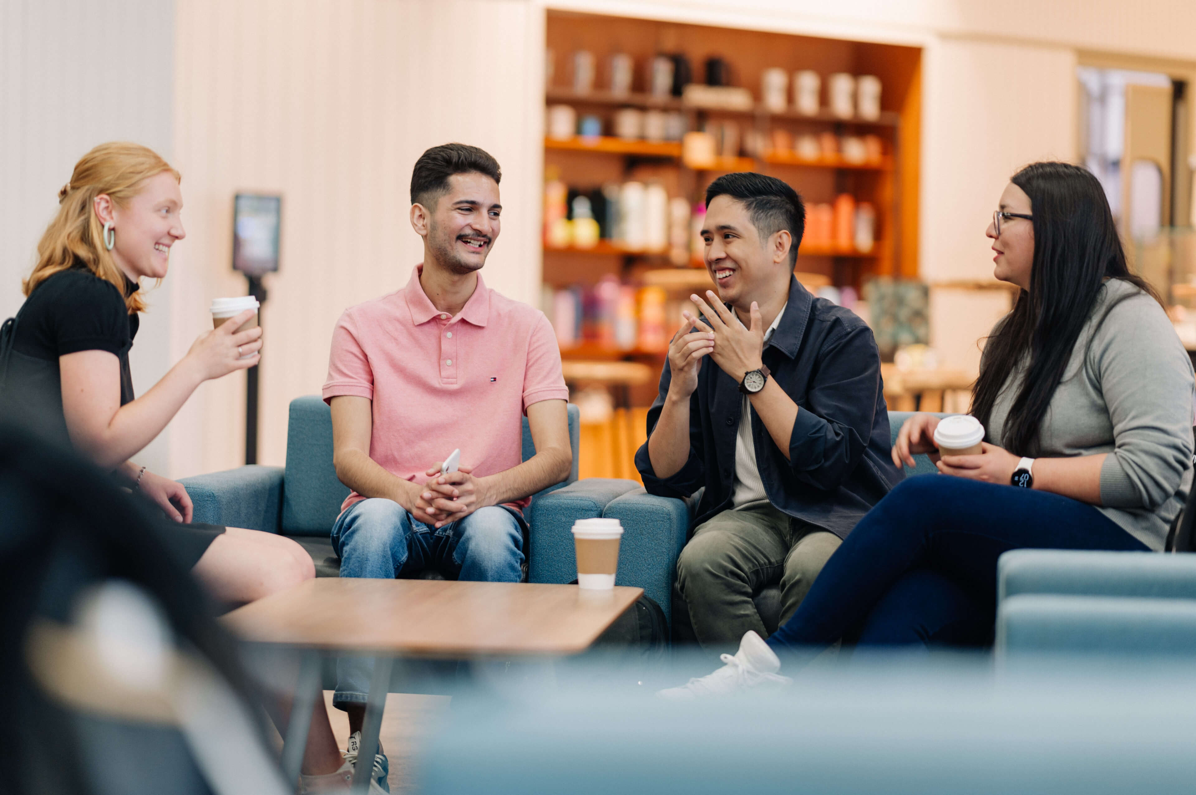A photo of four students sitting, laughing and holding coffee cups.