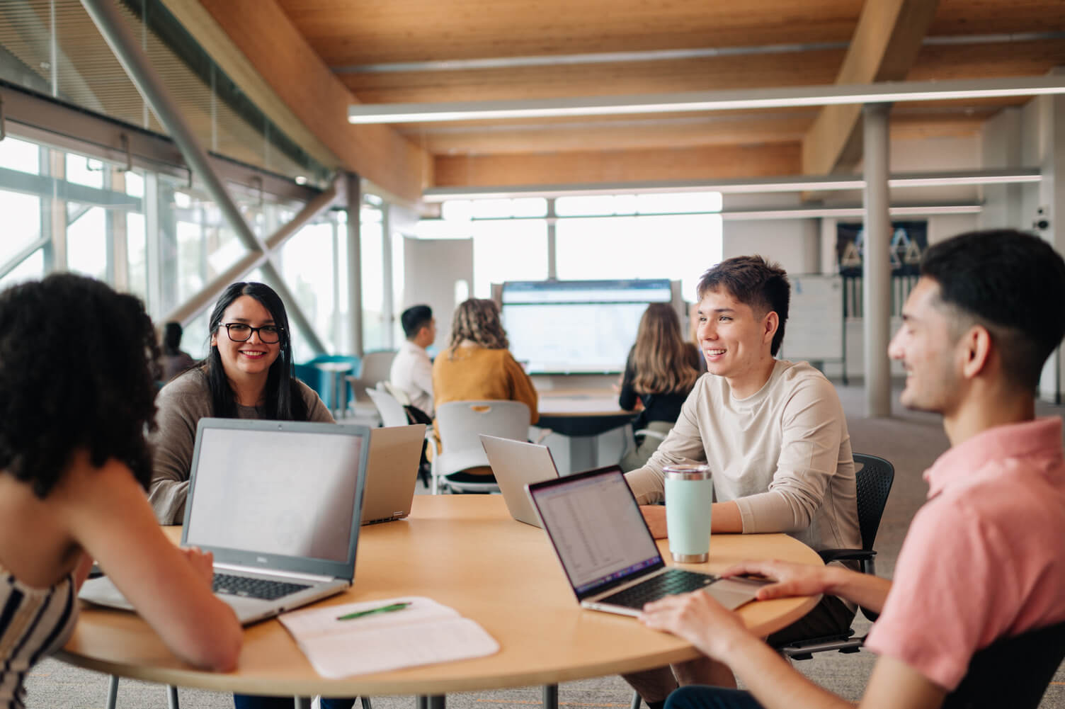 A photo of four students sitting around a table smiling and using their laptops.