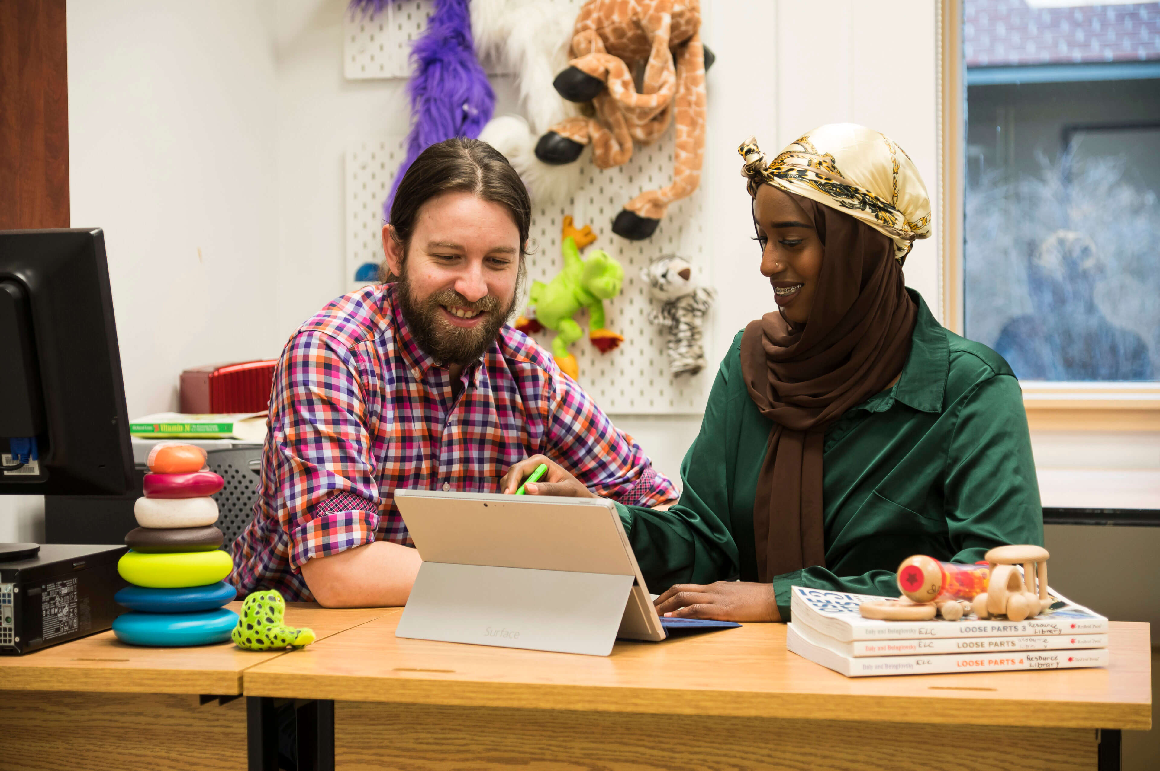 Two employees look at a computer tablet while surrounded by children's games.