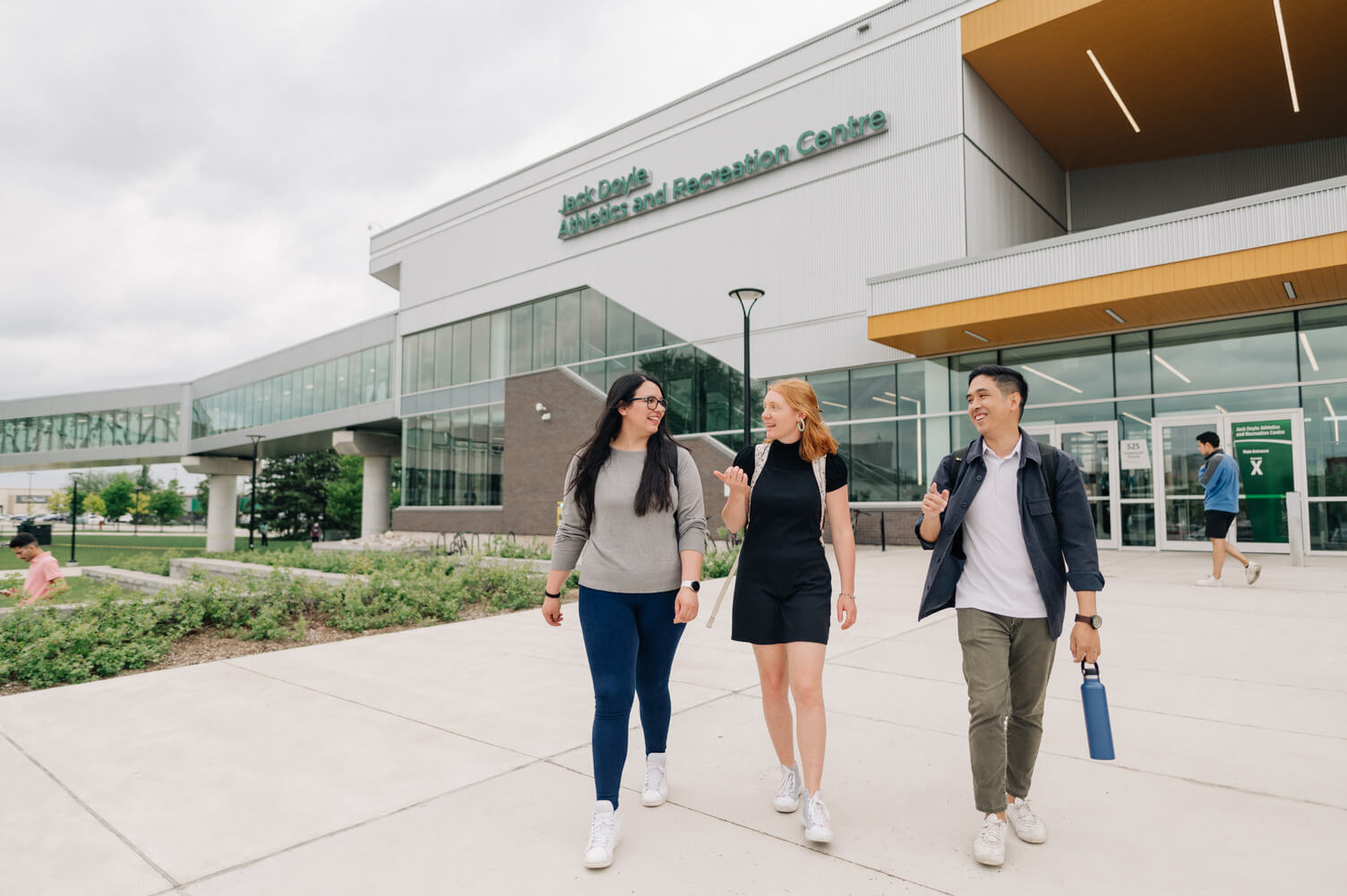 Three smiling students walk out from the Athletic Recreation Centre at Algonquin College.