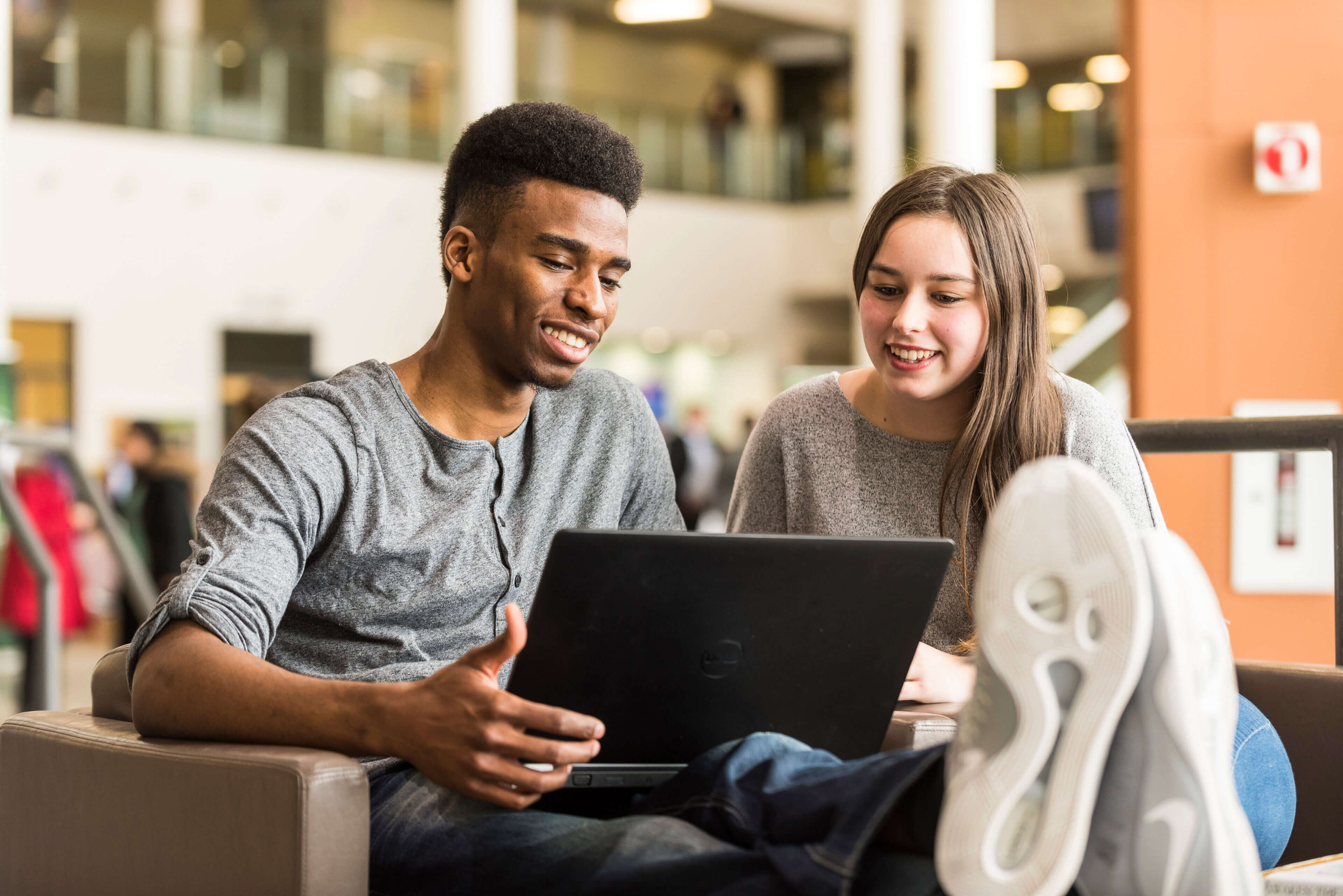 Two learners smiling and looking at a laptop.