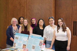 Seven women standing and smiling behind a table with displays.