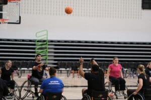 Women and men playing wheelchair basketball in the gym.