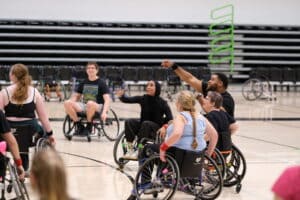 Women and men playing wheelchair basketball in the gym.